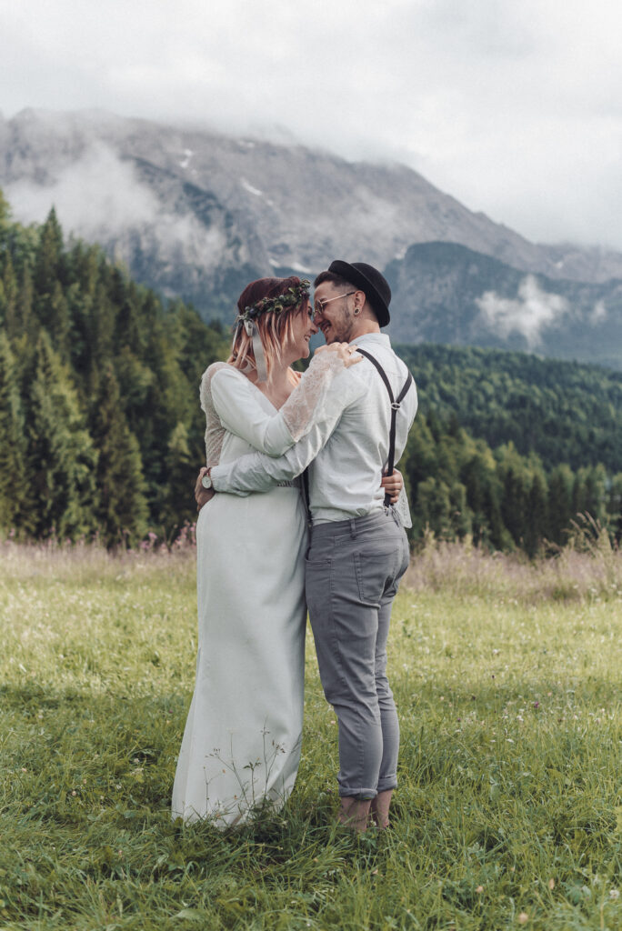 Alpine Boho-Hochzeit mit Blumen-Haarkranz in Beerentönen zum Boho-Brautkleid, Bräutigam mit Hut