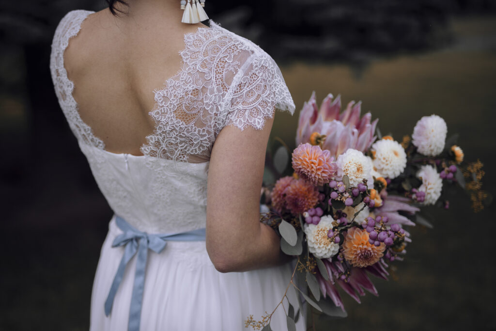 modernes Brautkleid in A-Form mit Spitzenelementen, Brautstrauß mit Dahlien und Protea