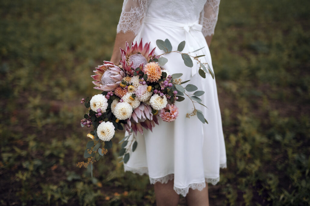 Brautstrauß mit Dahlien und Protea sowie Eukalyptus, kurzes Brautkleid mit Spitze